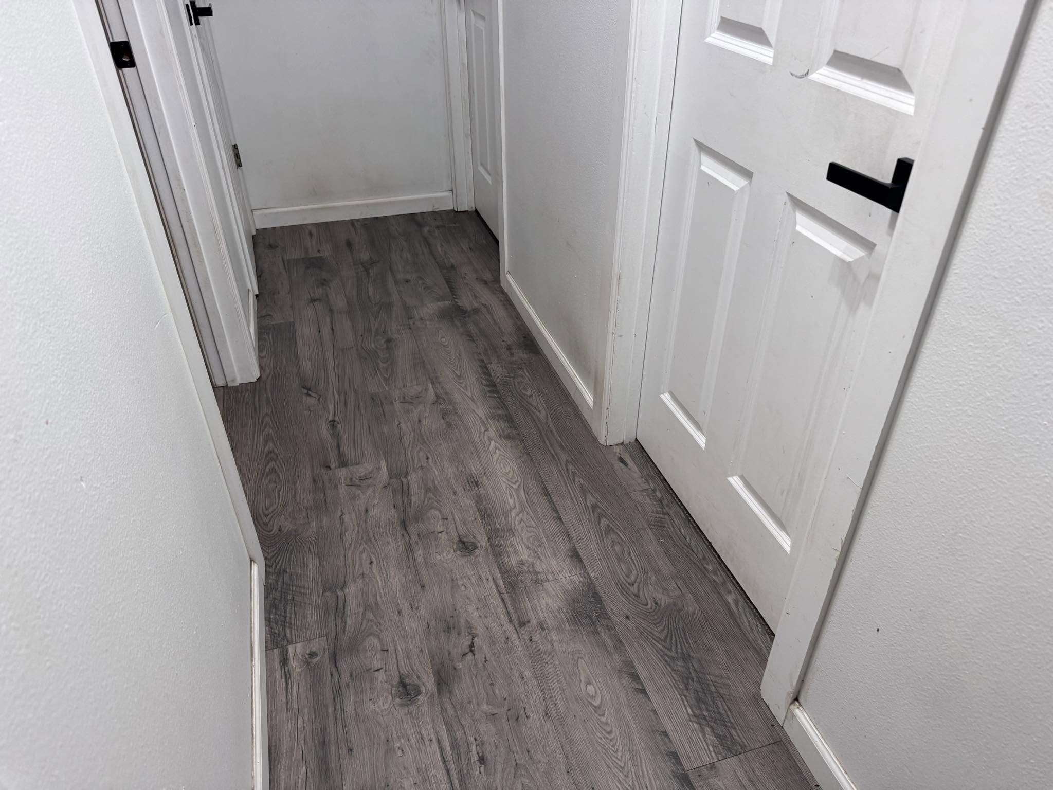 Gray vinyl-plank hallway flooring with white doors and black hardware
